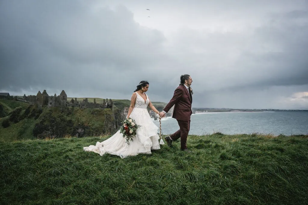 The couple holding hands in front of Dunluce Castle during their elopement