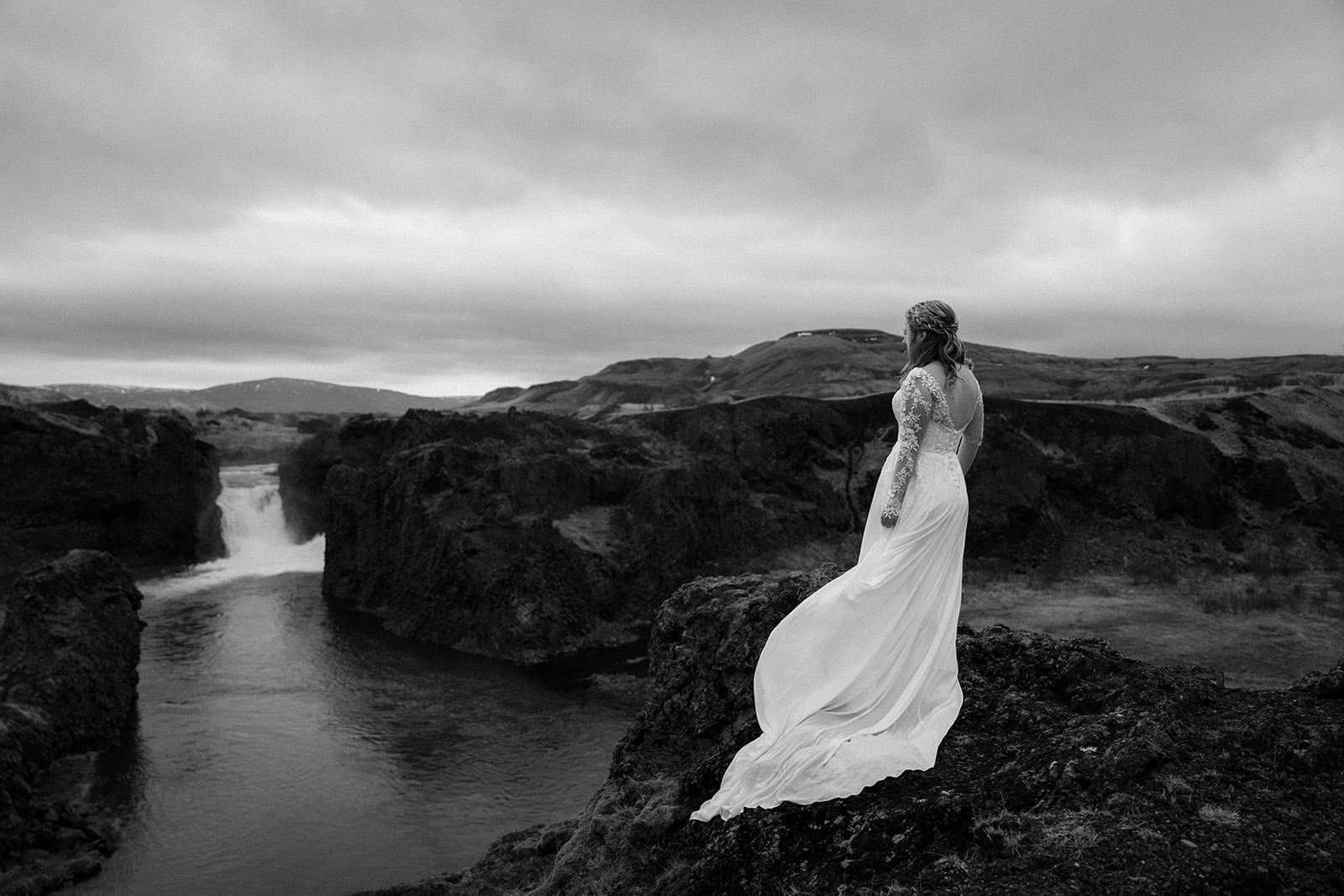 The bride’s wedding dress flowing in the wind by the waterfall at an Iceland elopement