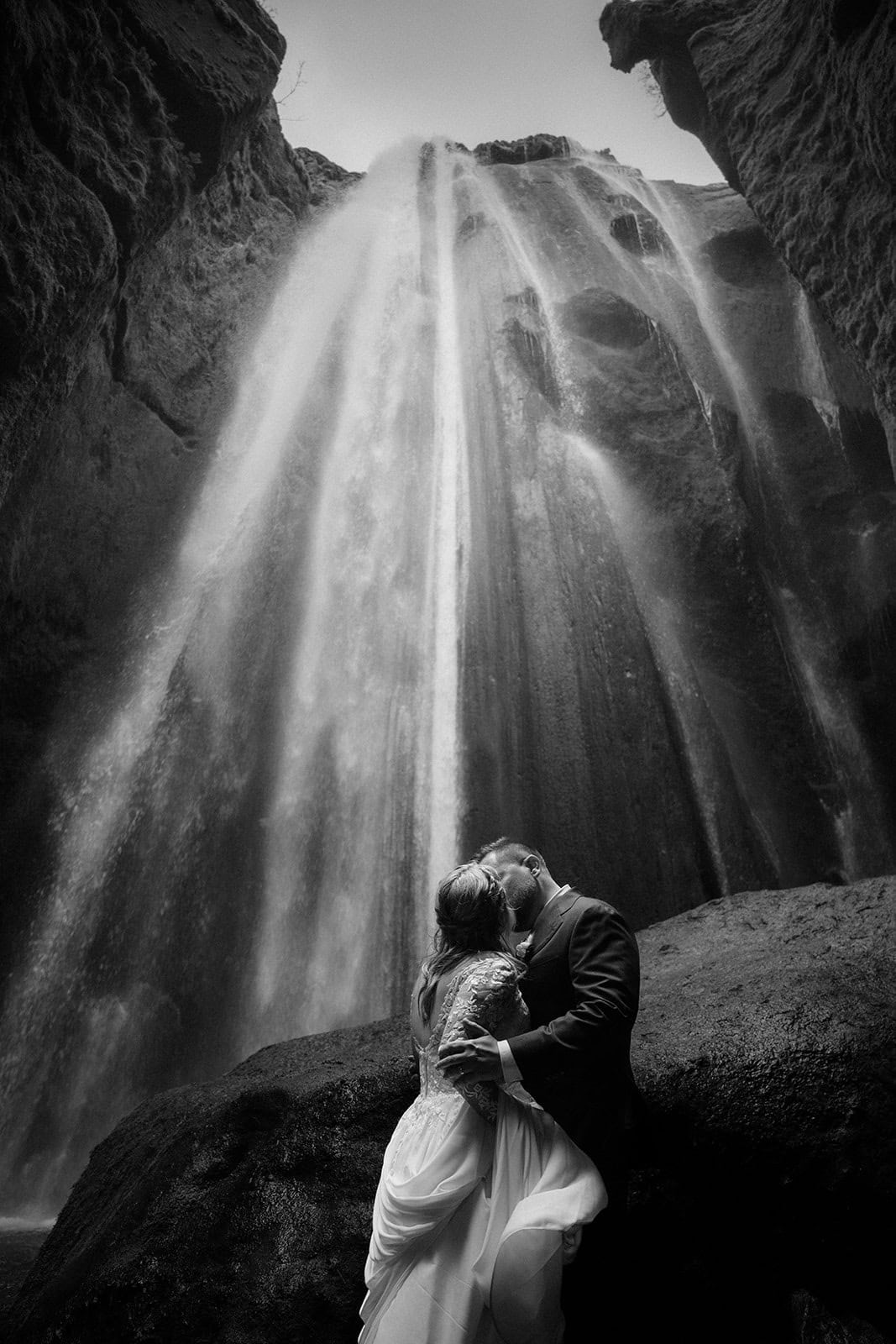 Bride and groom embracing in front of a waterfall during their Iceland elopement