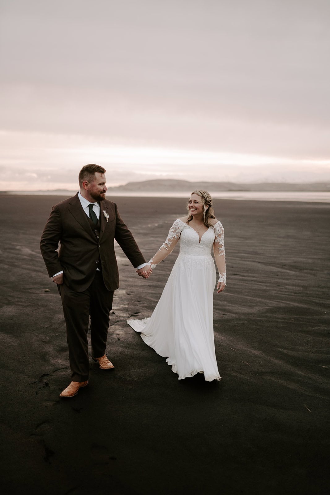 A wide view of the Icelandic landscape with the couple on a black sand beach during their elopement