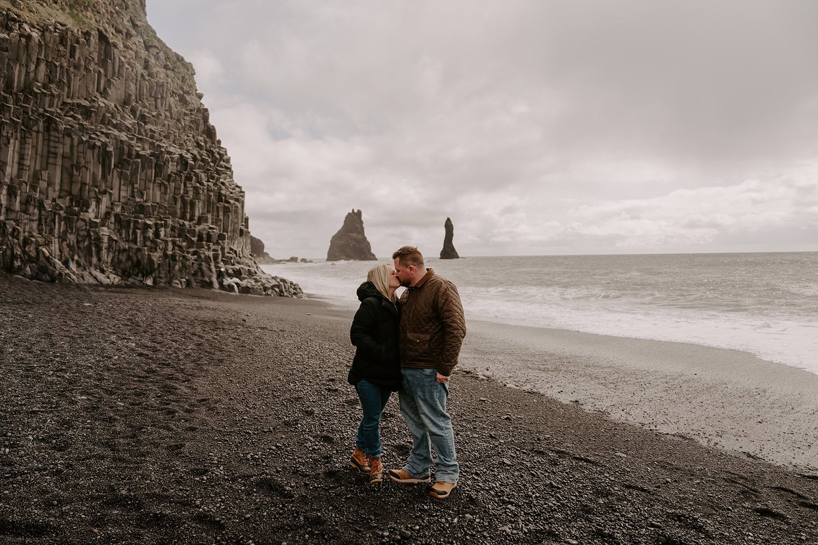 The couple walking along a rocky black sand beach at their Iceland elopement