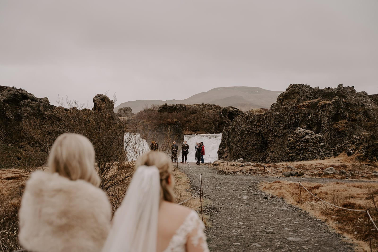 Iceland waterfall elopement with the bride walking through the ceremony place, framed by dramatic cliffs and falls