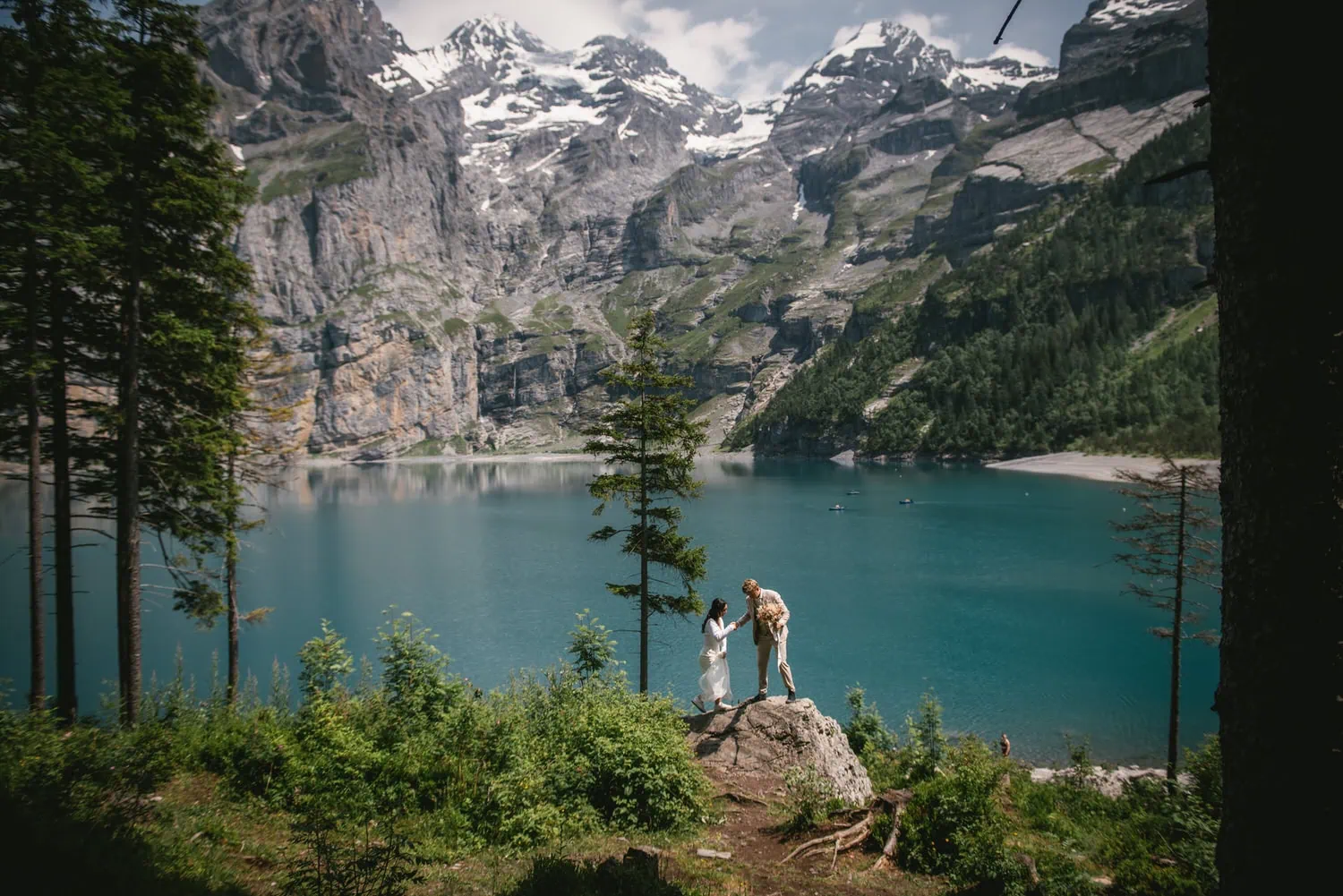 Elopement photo featuring a couple standing on a rock by a stunning mountain lake in Canada.
