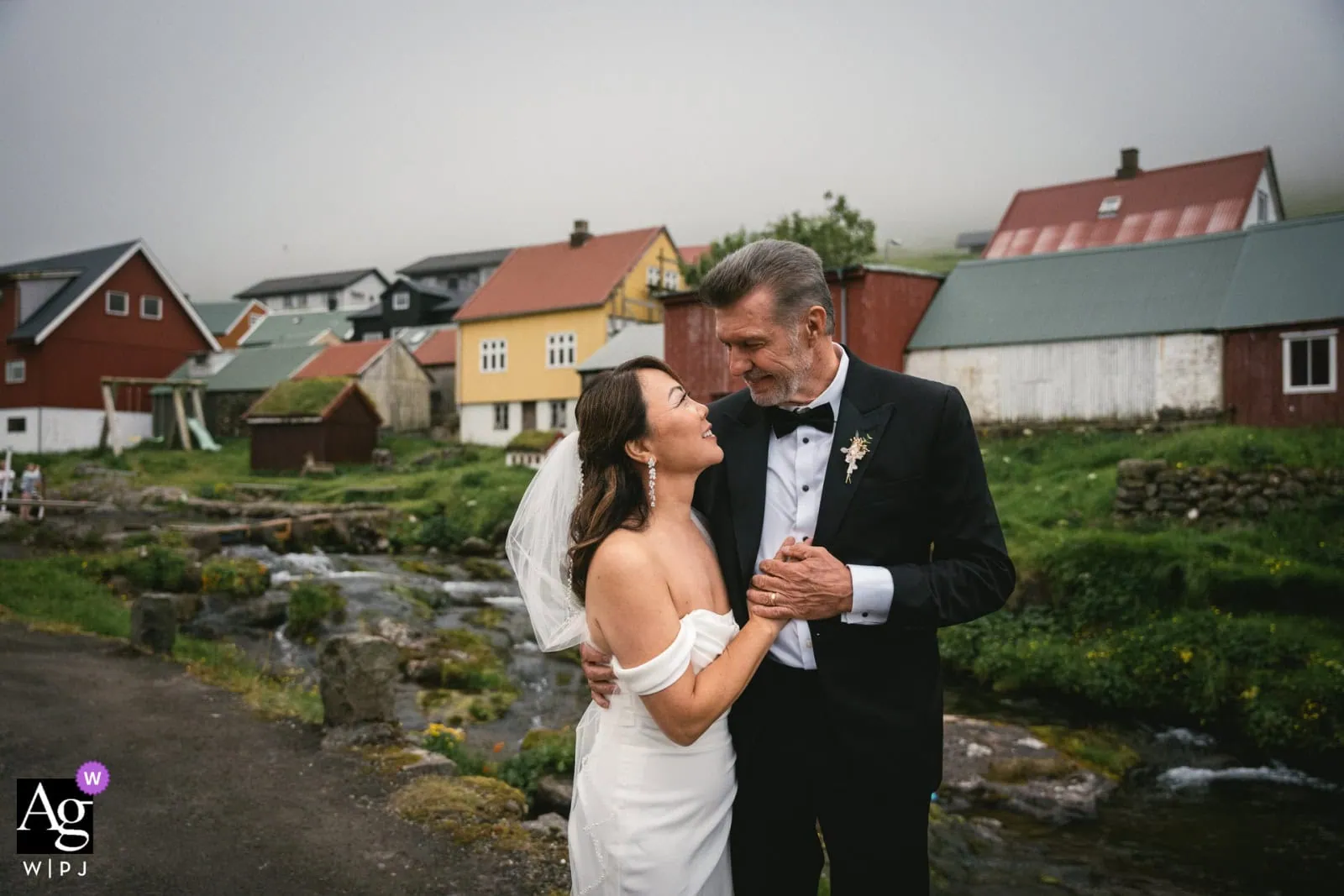 Romantic couple eloping in a picturesque village with colorful houses and a stream.