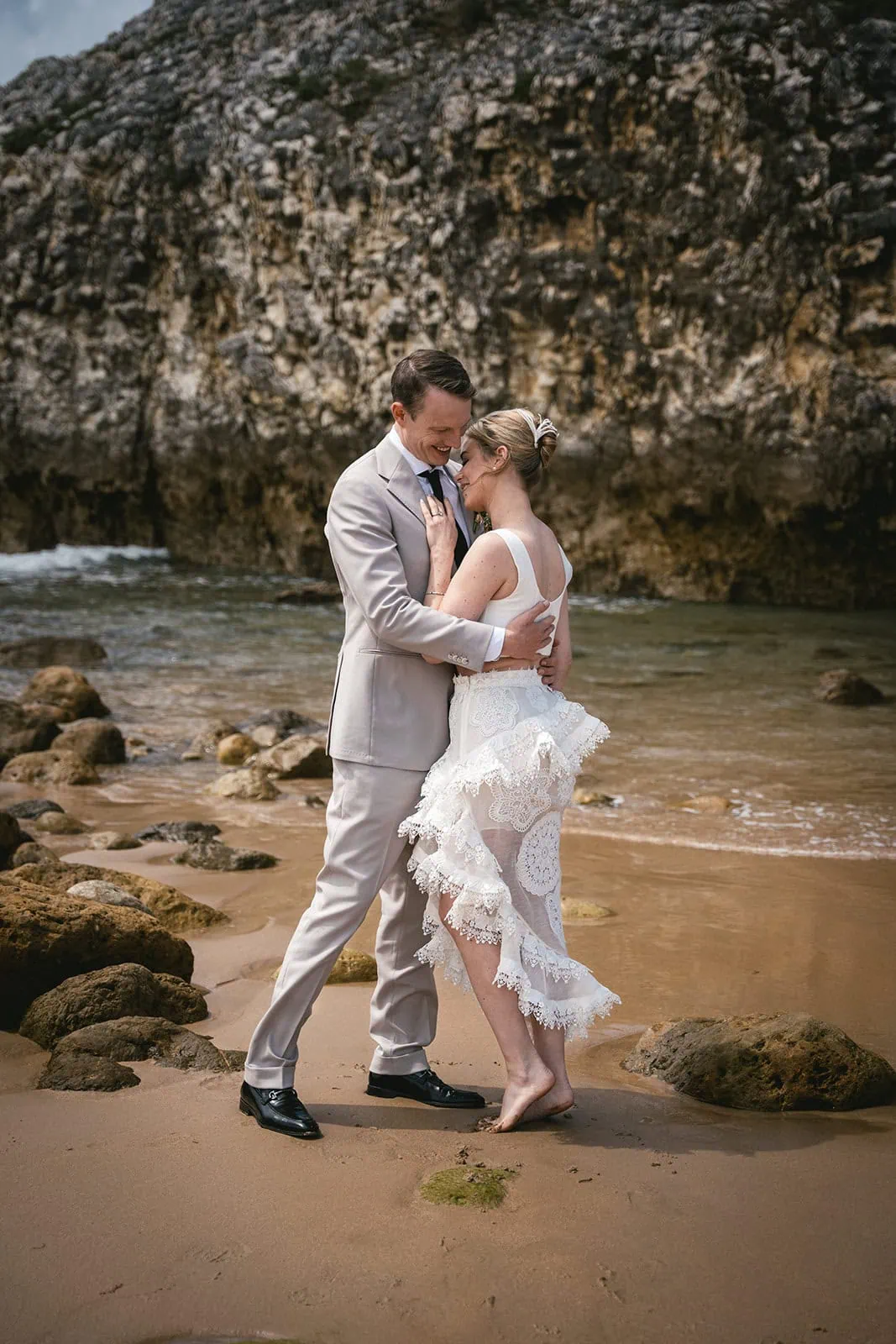 Groom embraces bride on the beach in this adventurous Spain elopement