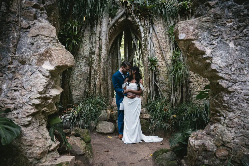 Real elopement couple embracing in mysterious Hawaiian ruins surrounded by lush jungle, sharing their authentic adventure story and review