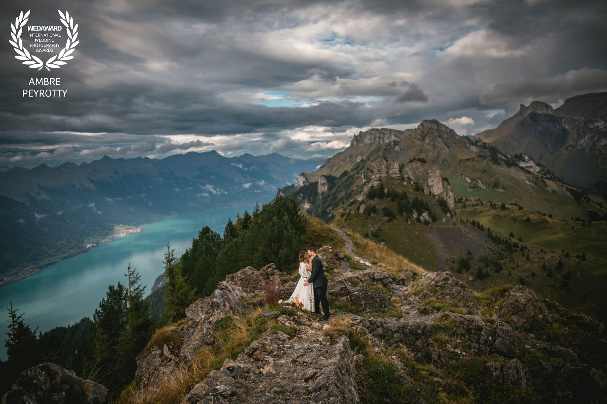 Distant couple embracing on mountain ridge overlooking turquoise alpine lake, highlighting the epic viewpoints in our New Zealand elopement packages