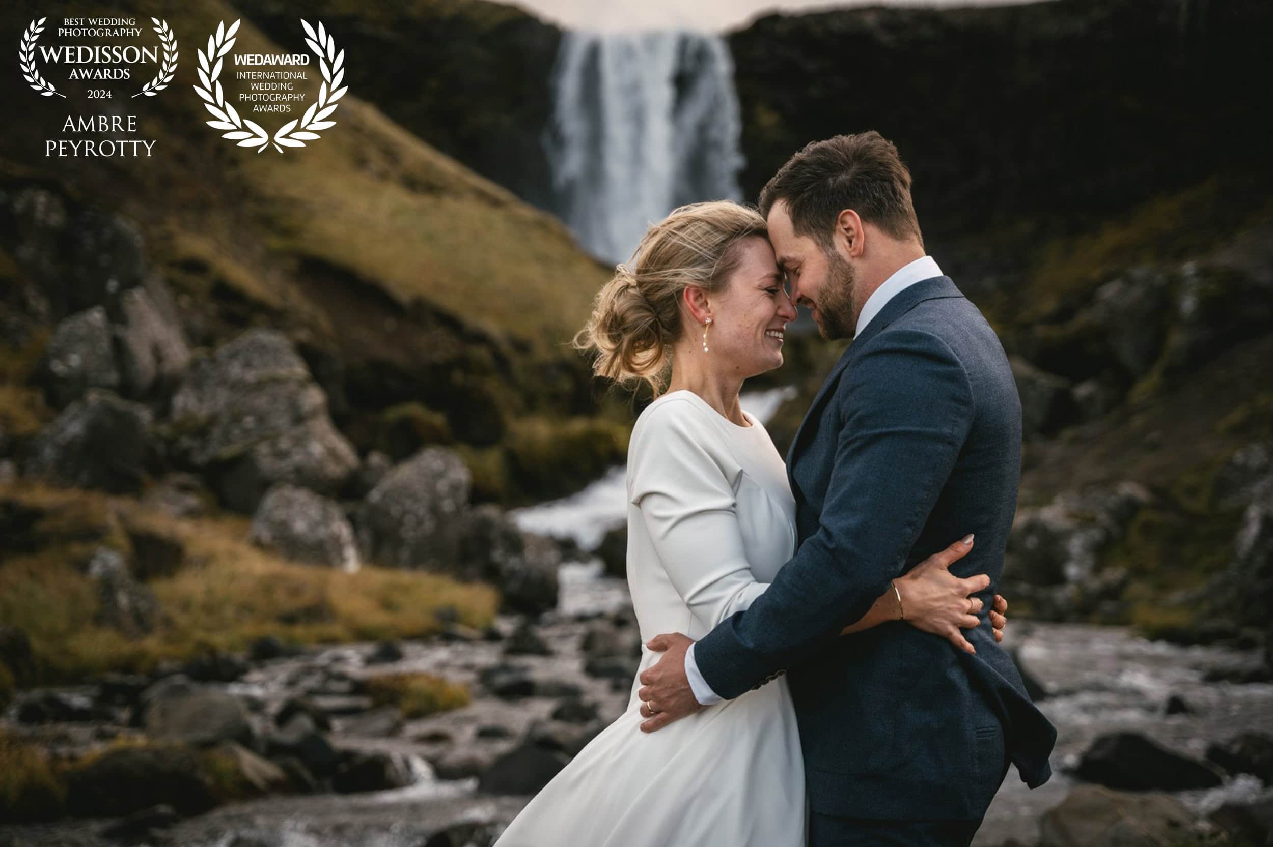 Couple embracing by powerful waterfall in New Zealand's iconic wind, showcasing the dramatic ceremony locations in our elopement packages