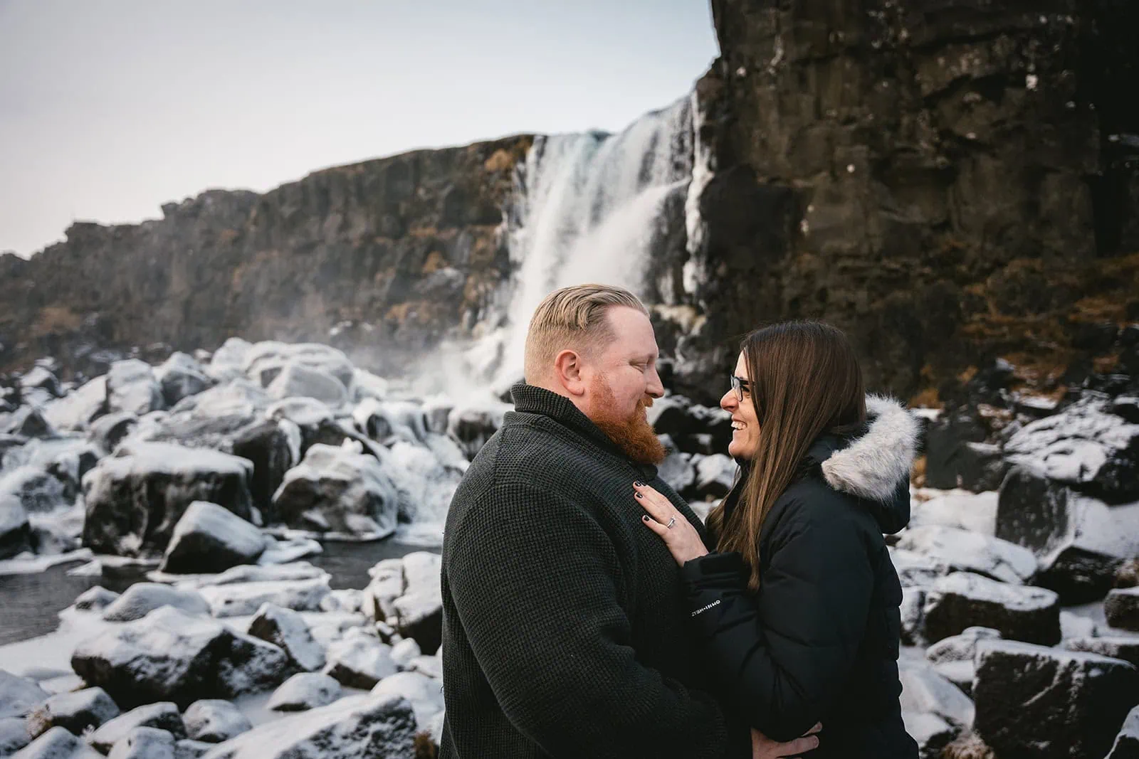 Gazing at each other by a snowy waterfall in their Vik elopement in Iceland
