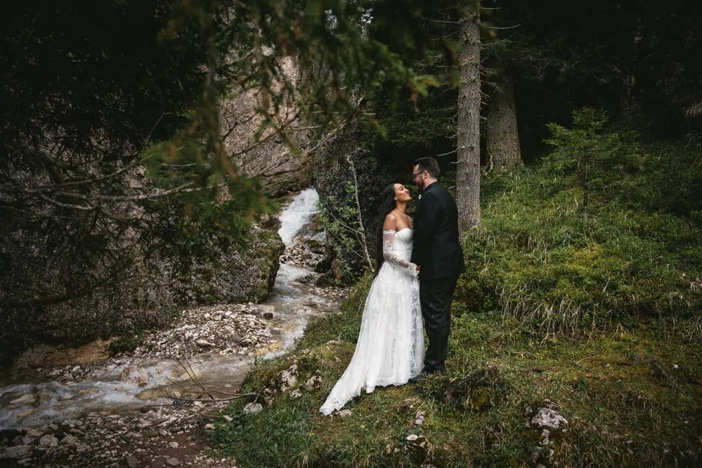 Dolomites elopement: Newlyweds gazing at each other near a tiny waterfall in the mountains
