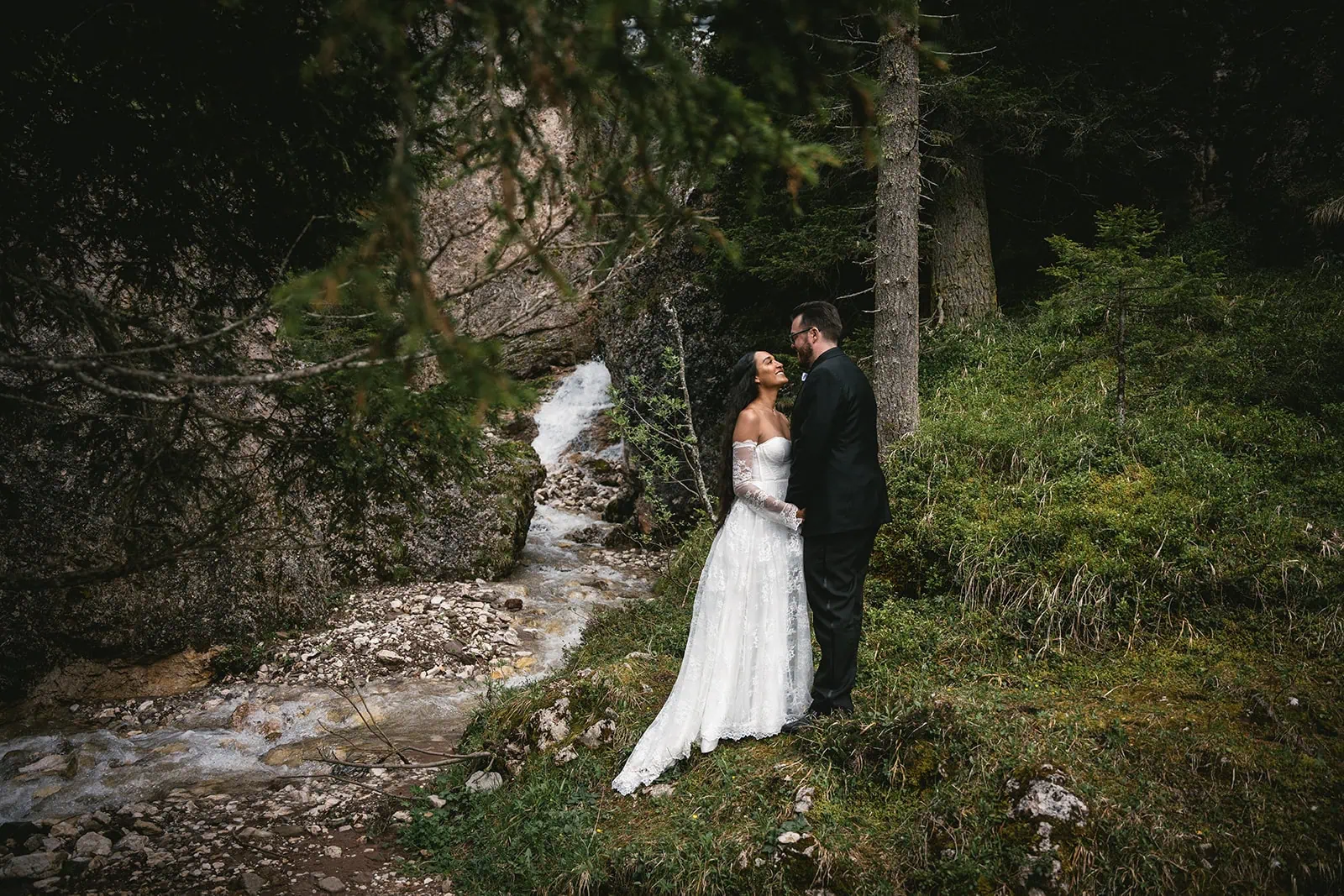 Dolomites elopement: Newlyweds gazing at each other near a tiny waterfall in the mountains
