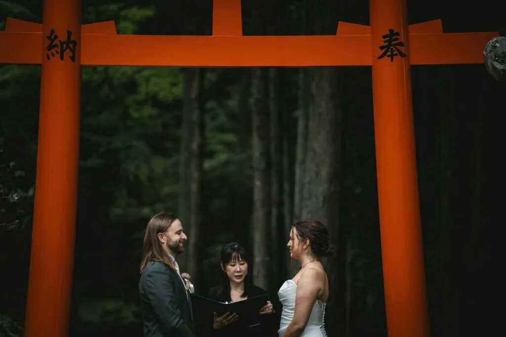 Elope in Japan under a traditional torii gate with a couple and officiant, capturing a romantic elop.