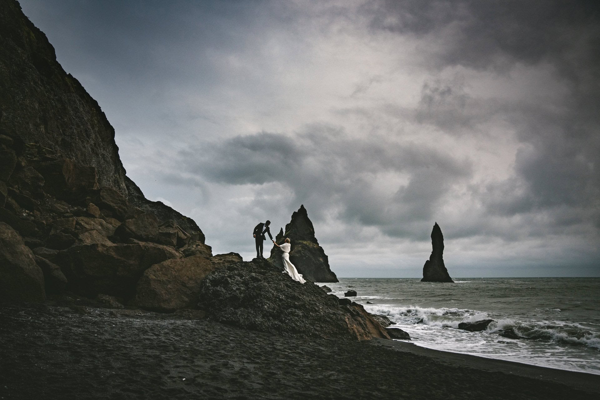 Bride and groom eloping on a black sand beach with basalt cliffs in Iceland