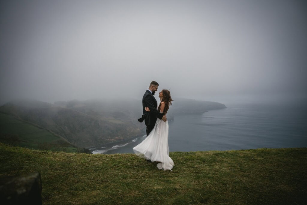 Romantic wedding couple embracing on scenic cliffs with ocean view, dreamy elopement.