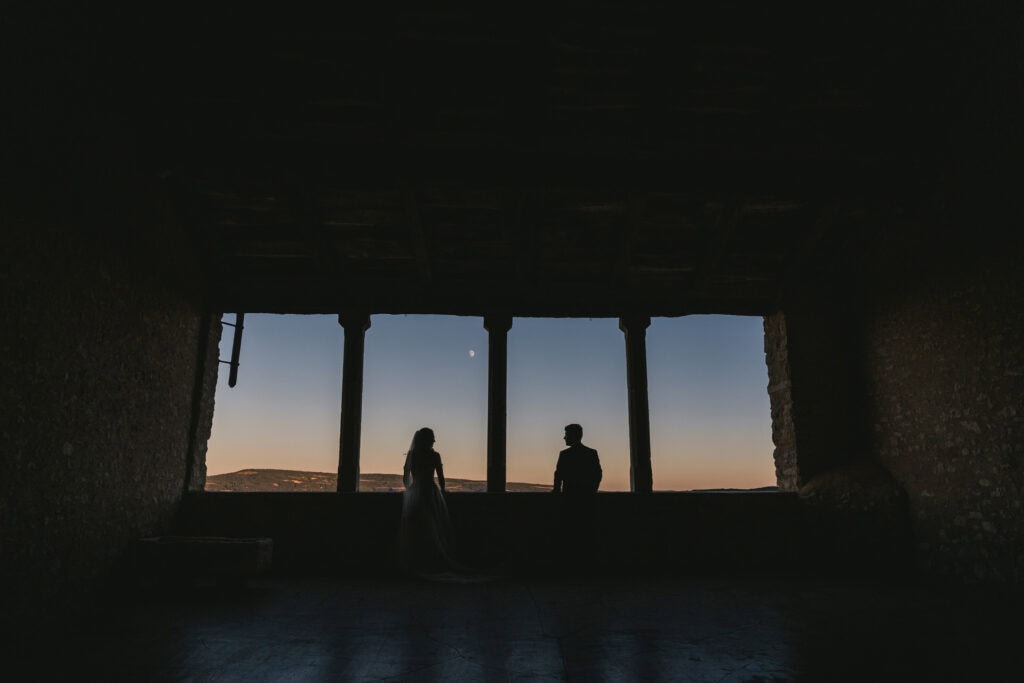 A couple's silhouette against sunset sky with moon, during an intimate elopement ceremony.