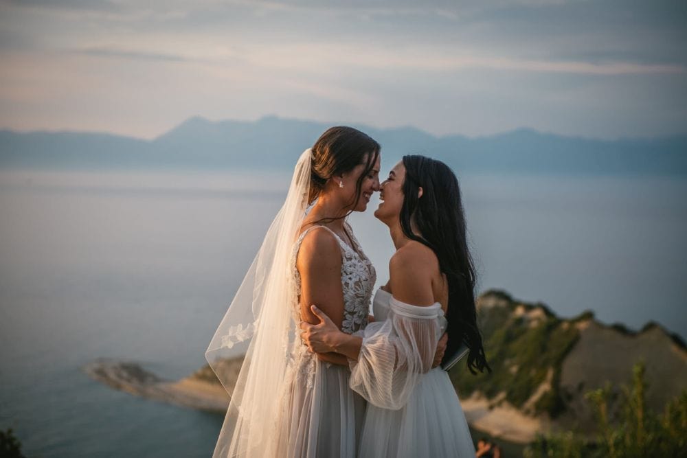 Elegant wedding couple embracing at sunset overlooking ocean cliffs.