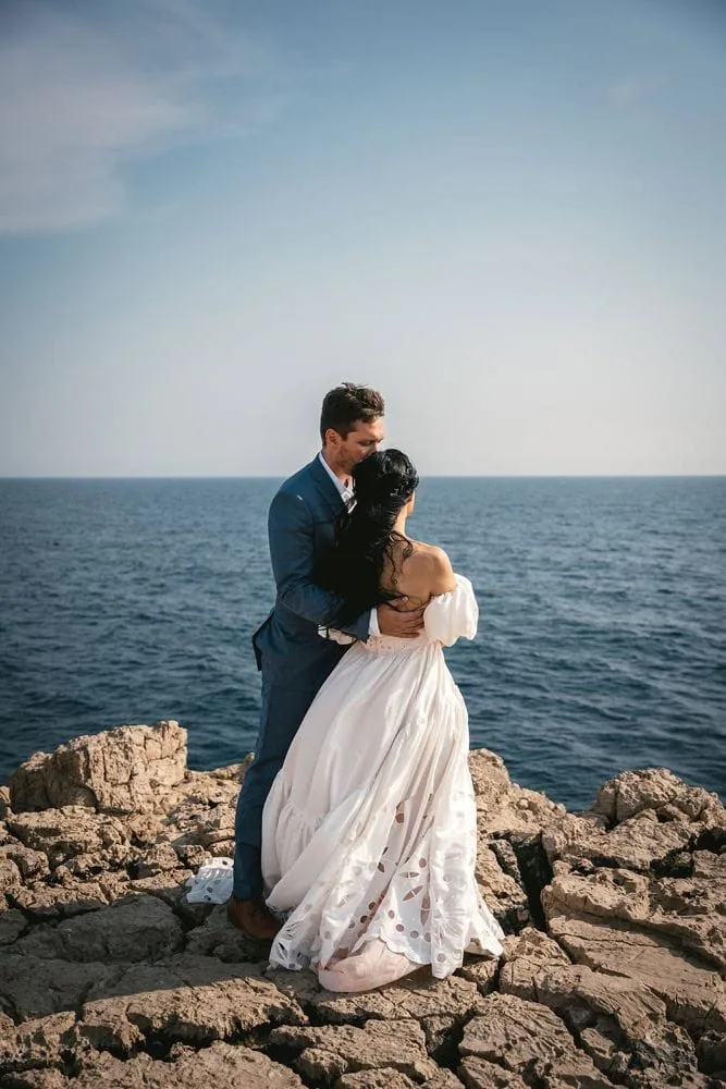 Elopement couple embracing on rocky coast with ocean backdrop in Hawaii.