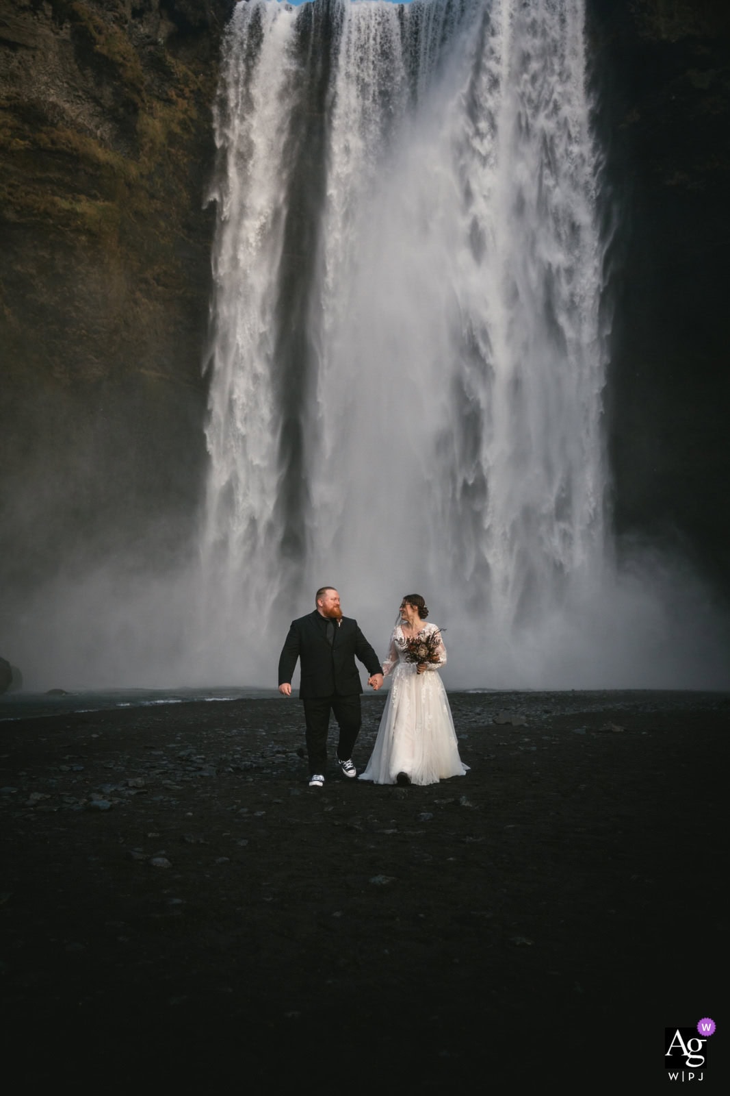Bride and groom holding hands at a stunning Iceland waterfall during their elopement.