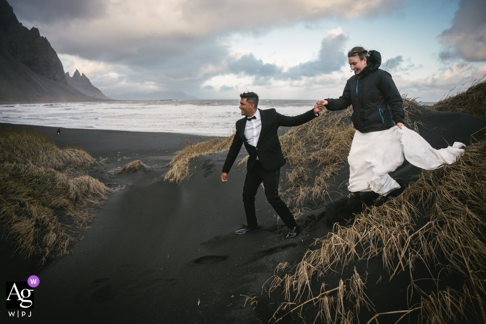 Elopement couple holding hands on Iceland's black sand beach with dramatic cliffs and cloudy sky in.