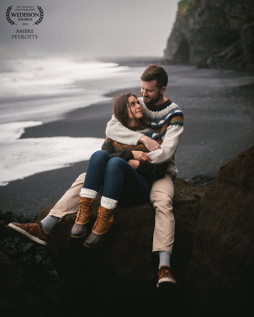 Romantic couple sitting on a black sand beach in Iceland, embracing during an elopement.