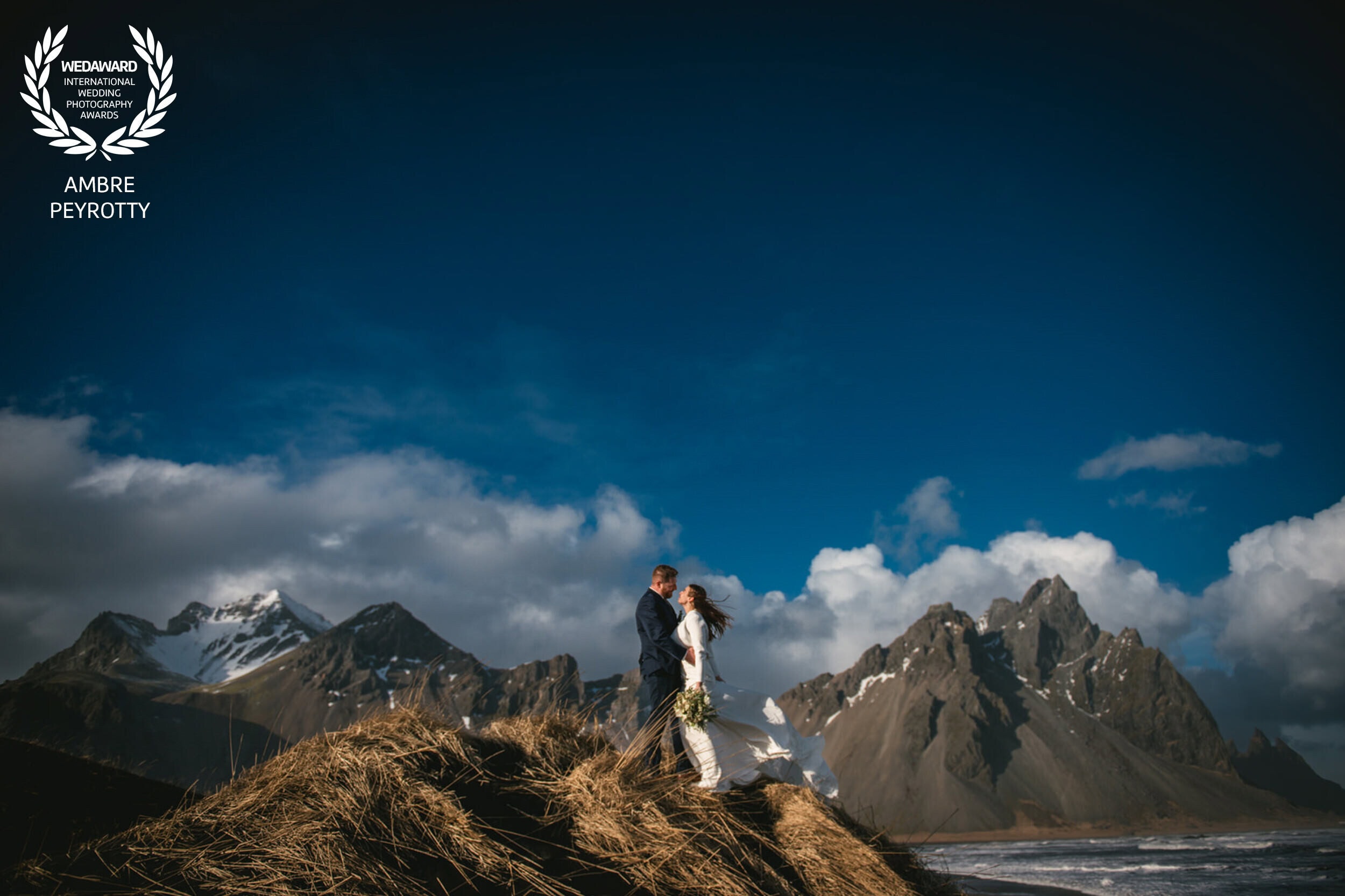 Elopement couple standing on a grassy hill with Icelandic mountains in the background.