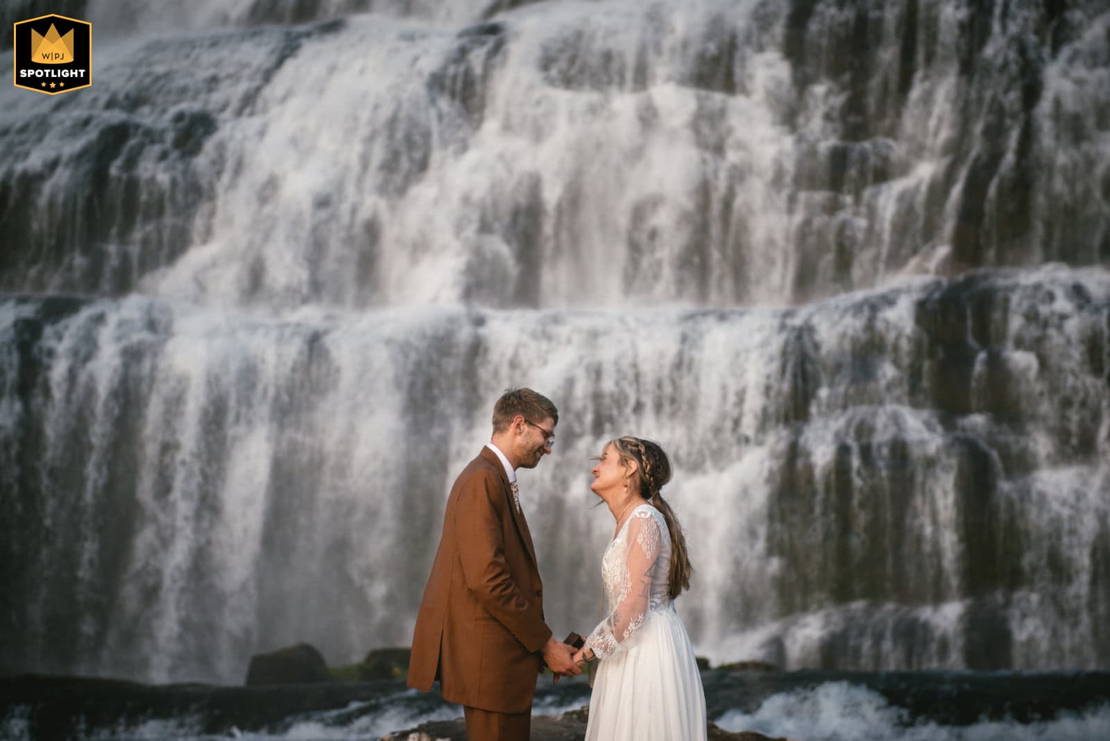 Romantic couple eloping at Iceland waterfall with cascading water backdrop.