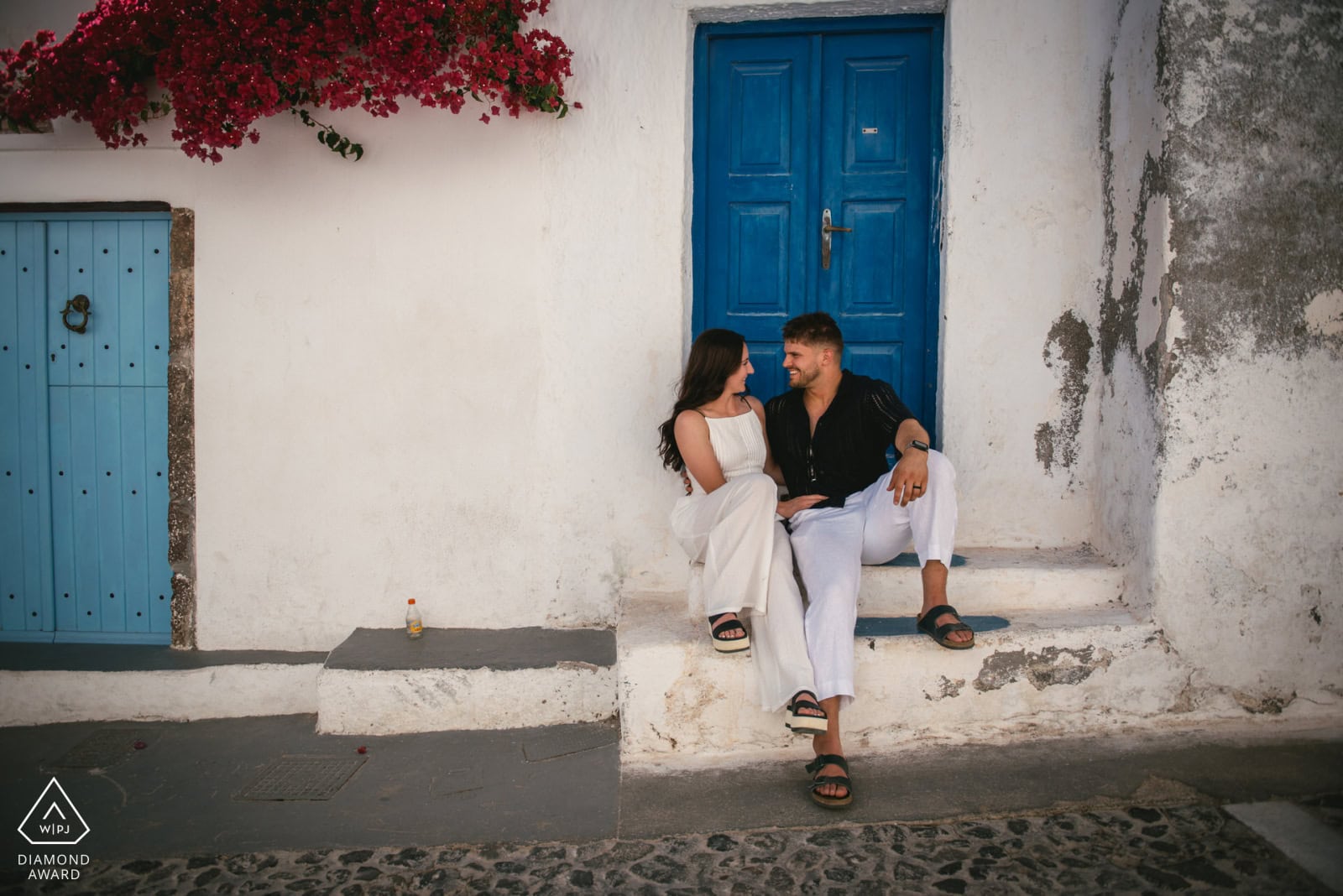 Elopement couple sitting on steps in Greece with white walls and blue door.