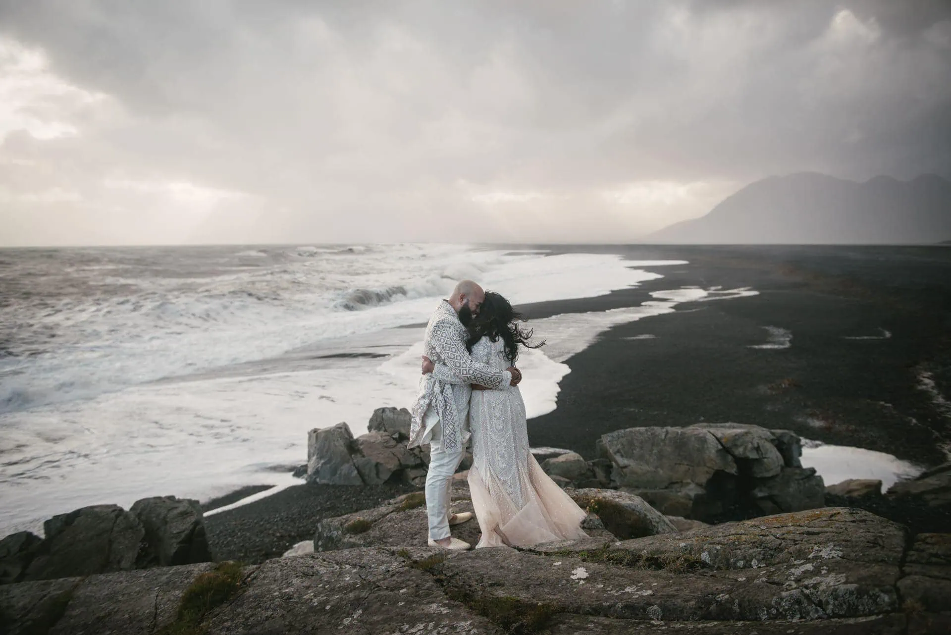 Romantic Iceland elopement on black sand beach with ocean waves and dramatic sky.