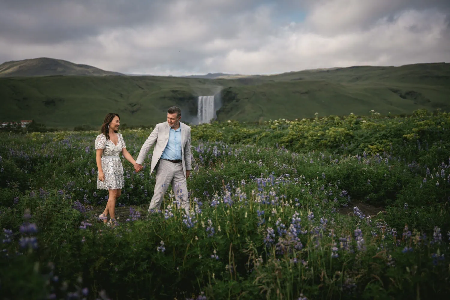 Elopement couple walking in Icelandic fields with waterfall backdrop.