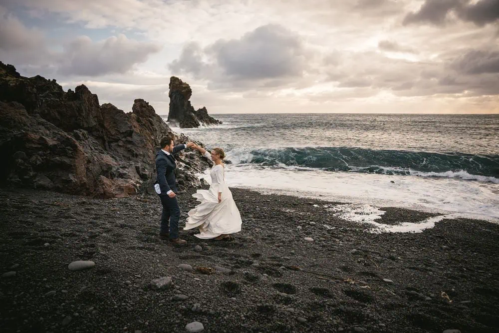Romantic Iceland elopement on a black sand beach with ocean waves and rocky cliffs.