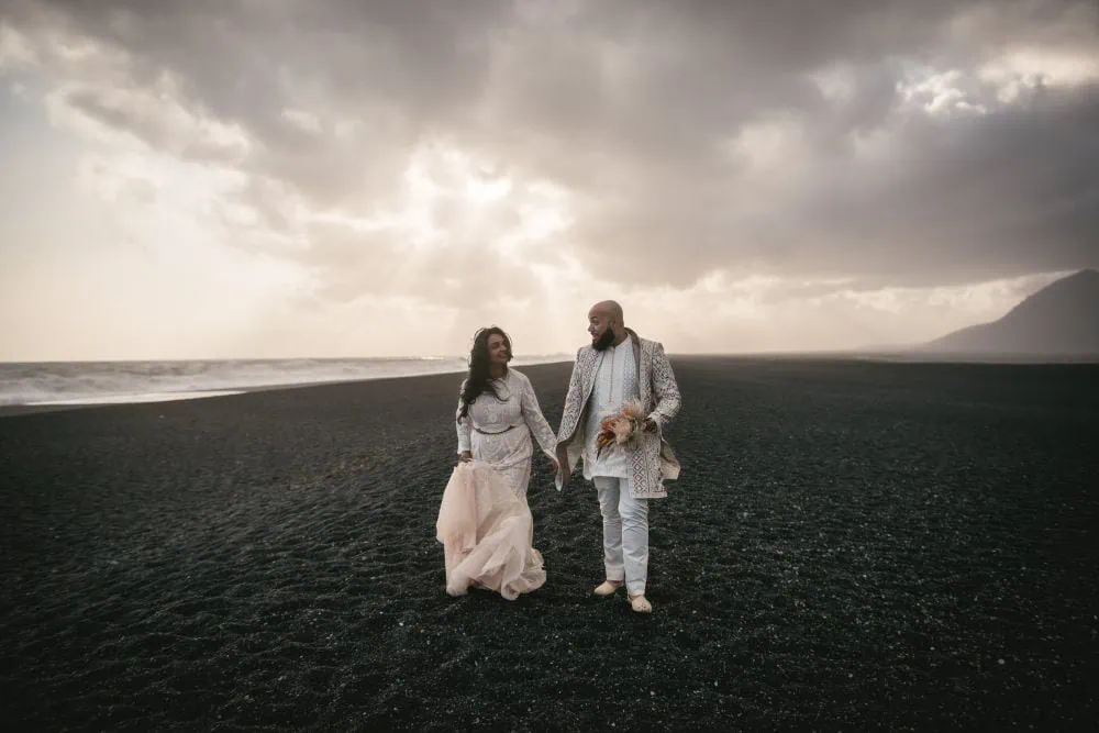 Elopement couple walking on black sand beach in Iceland at sunset.