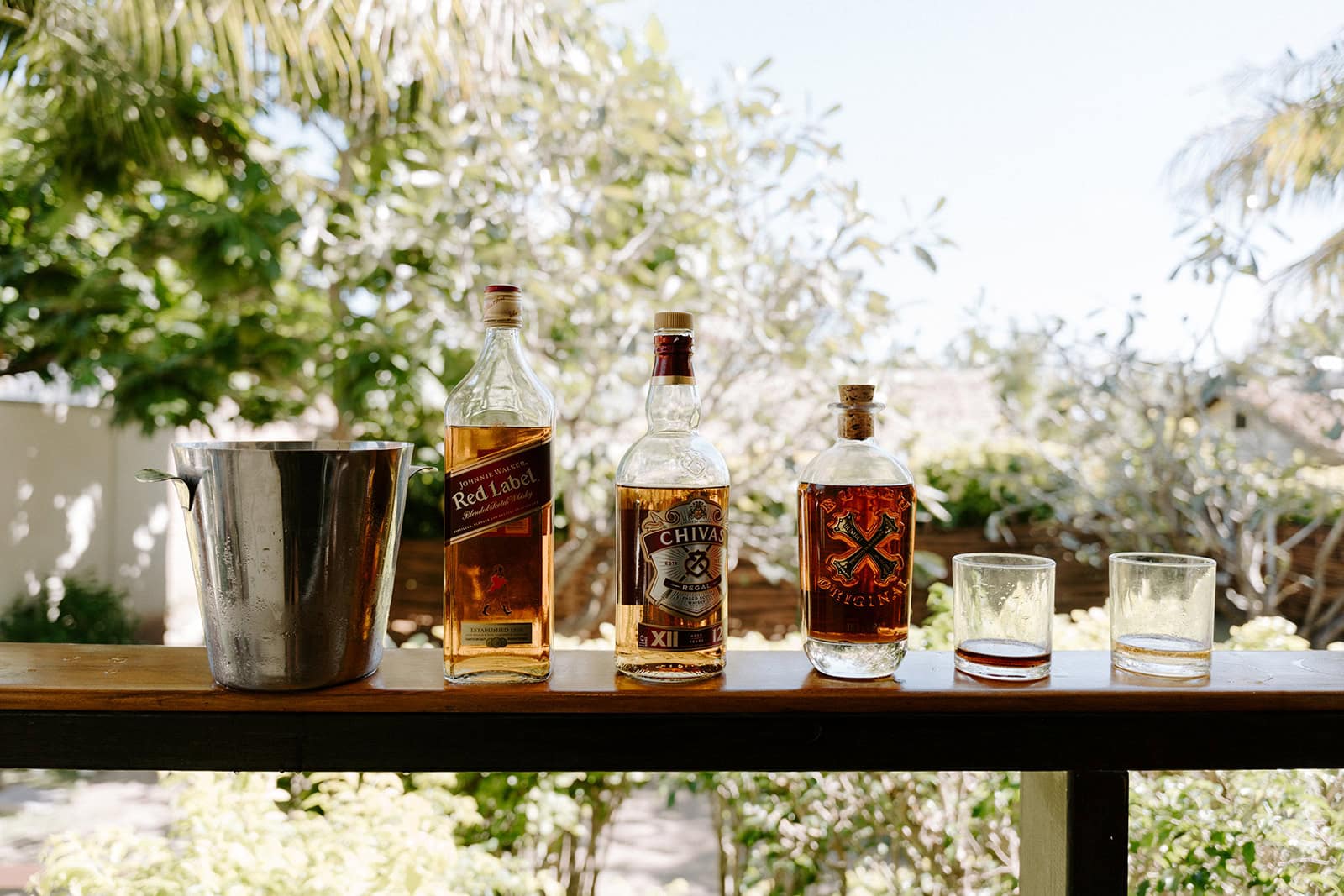 Elopement celebration with liquor bottles and glasses on a wooden table outdoors.