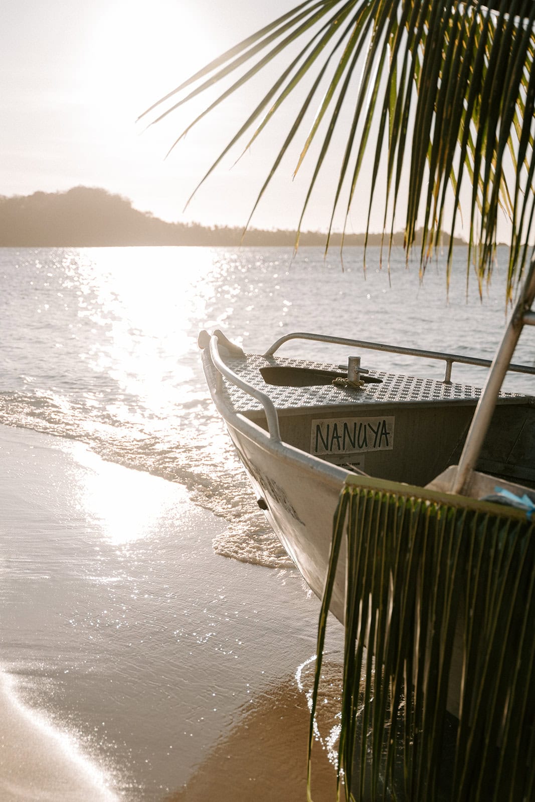 Boat on the beach with palm leaves, sunset reflection, tropical paradise scene.