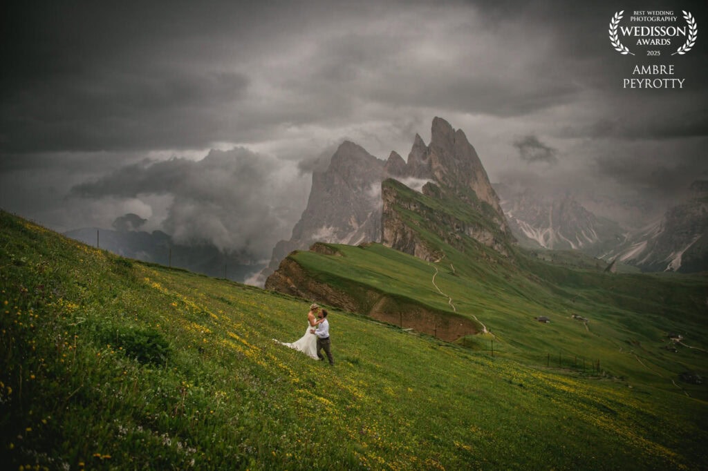 Elopement couple embracing on lush green hillside with dramatic mountain backdrop in Italy.