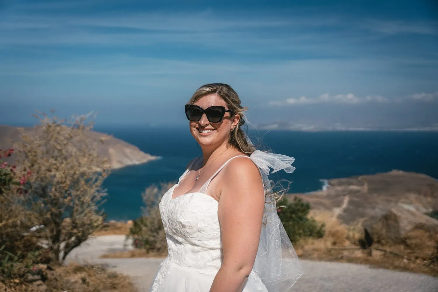 Bride in wedding dress smiling with ocean and sunset in background on Paros, Greece.