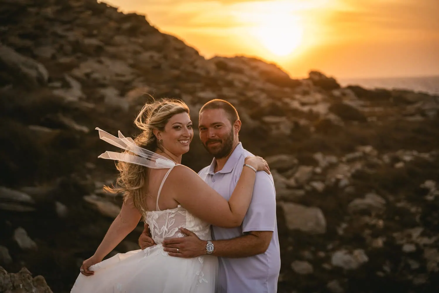Elopement couple at sunset on Paros, Greece, with rocky landscape and warm sunset glow.