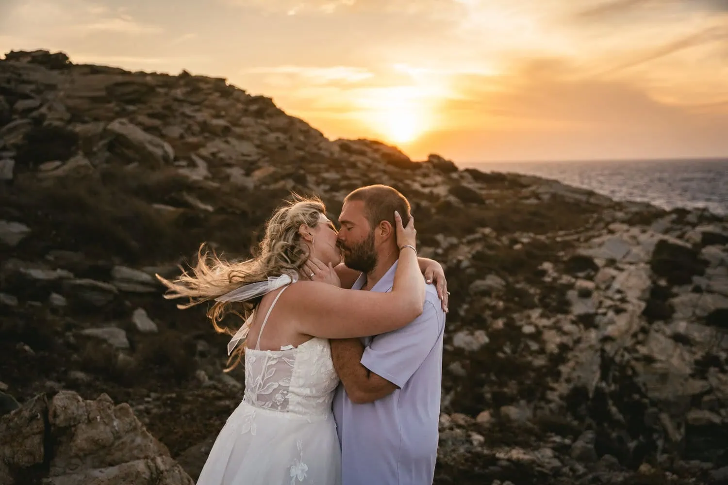 Romantic couple during sunset elopement on Paros, Greece, with rocky landscape background.