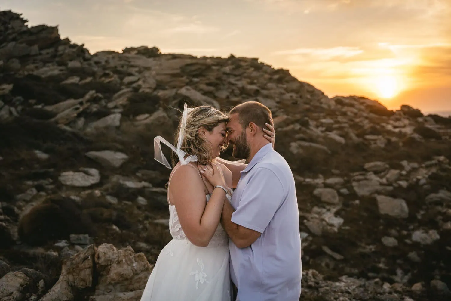 Romantic couple during sunset elopement on Paros, Greece, with rocky landscape background.
