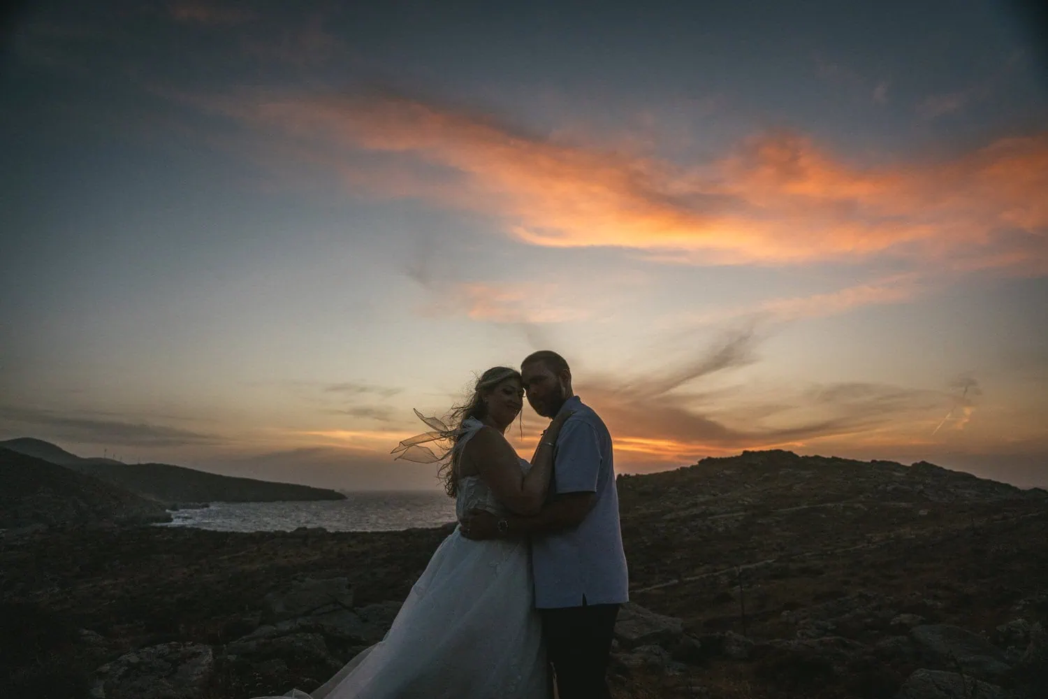 Elopement couple at sunset on Paros, Greece, with stunning sky and ocean backdrop.