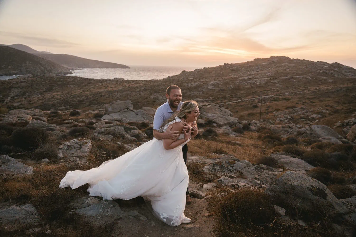 Elopement couple embracing at sunset on rocky terrain in Paros, Greece.
