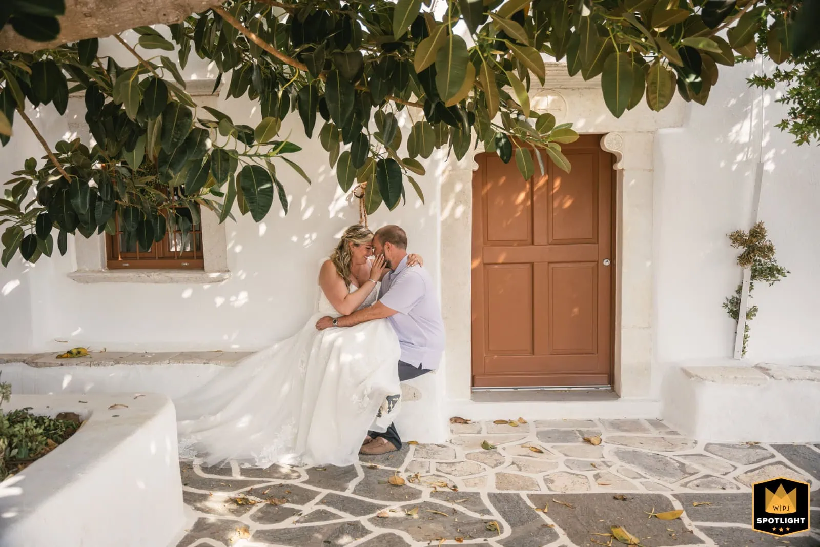 Elopement couple under a tree with white walls and wooden door in Greece.