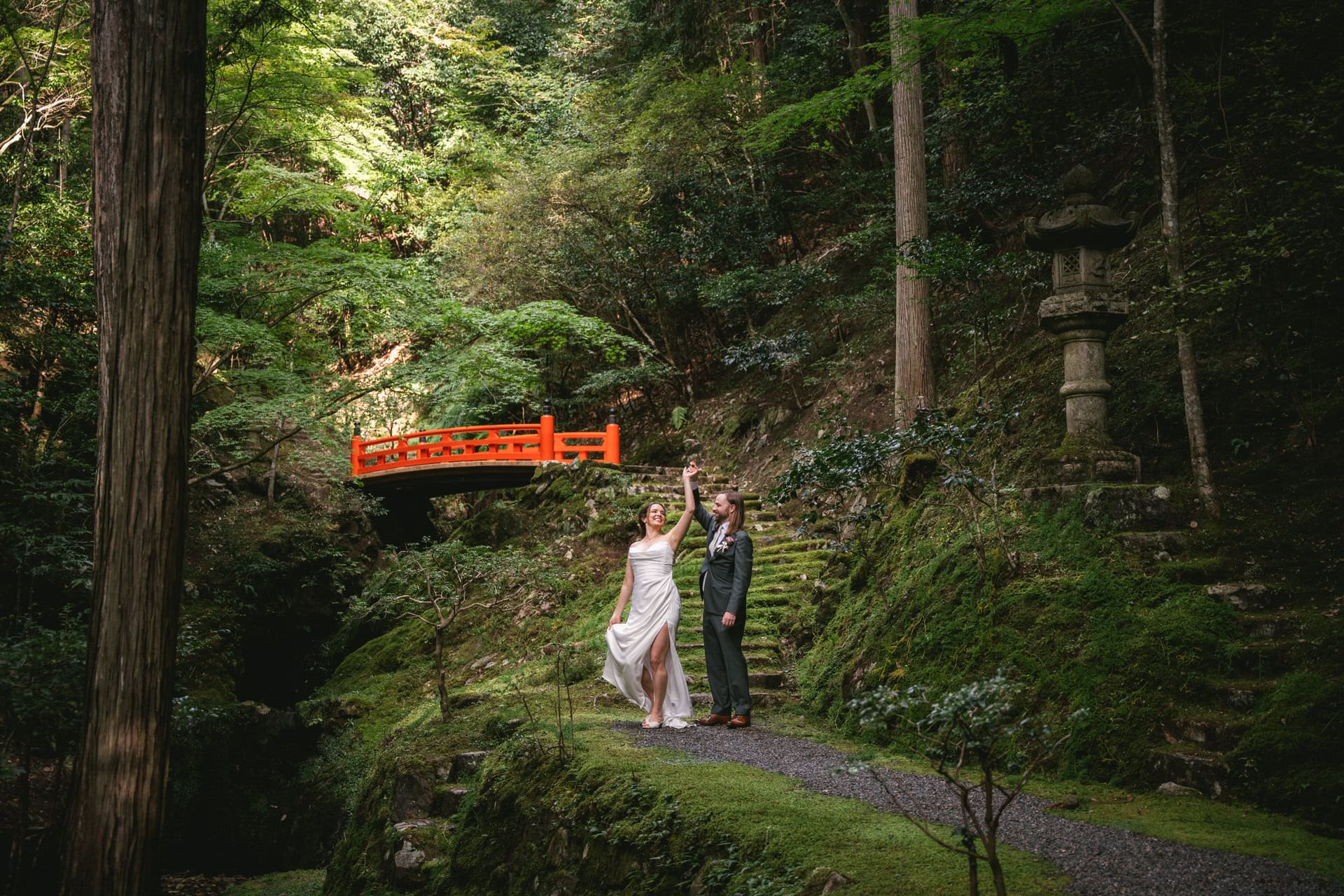Elopement couple standing on a forest path with lush greenery and traditional Japanese lanterns.